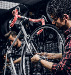 Two attractive repairmans are fixing broken bicycle at their dark workshop.